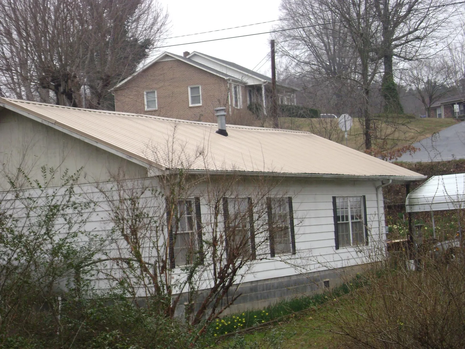 Tan metal roof on a white sided house set into a hillside — Commercial Roofing by Roofing Brothers in Solana Beach